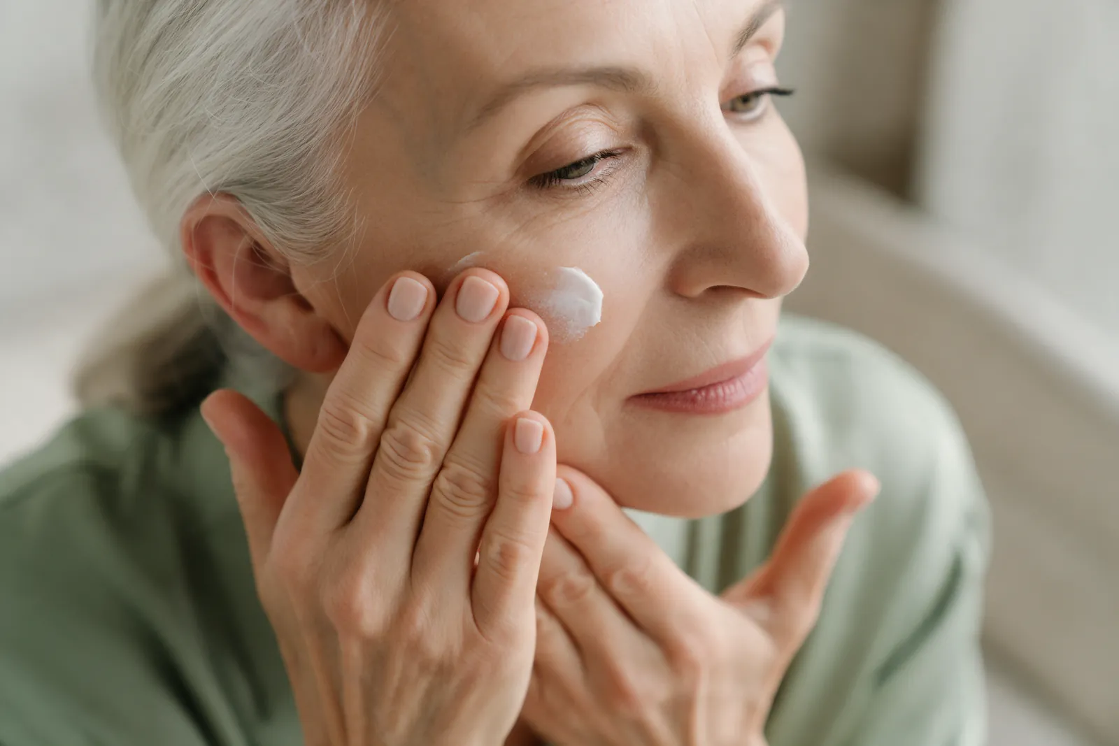 Mains d'une femme de 60 ans appliquant une crème après une brume d'eau florale, lumière naturelle