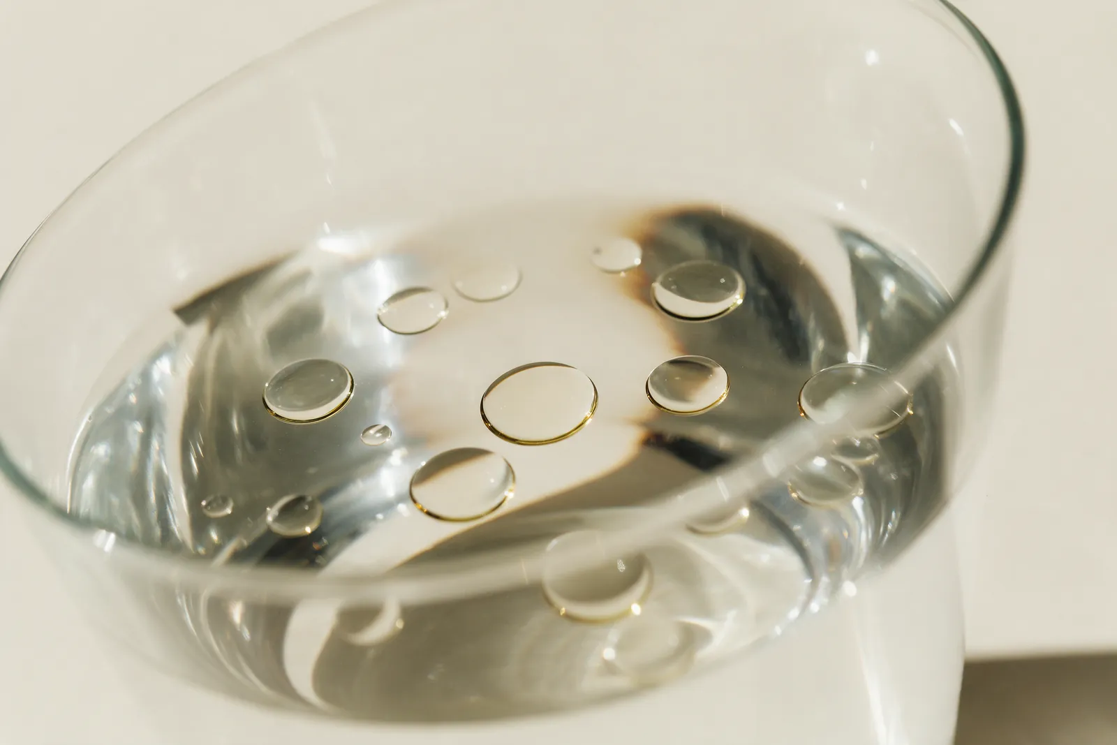 Gouttes d'huile essentielle flottant à la surface de l'eau dans un verre transparent, gros plan