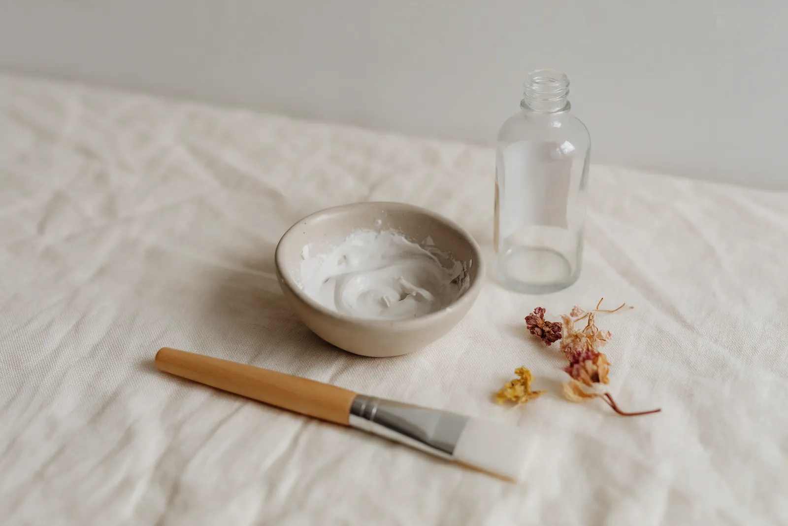 Petit bol d'argile blanche délayée avec un hydrolat, pinceau à masque et flacon en verre